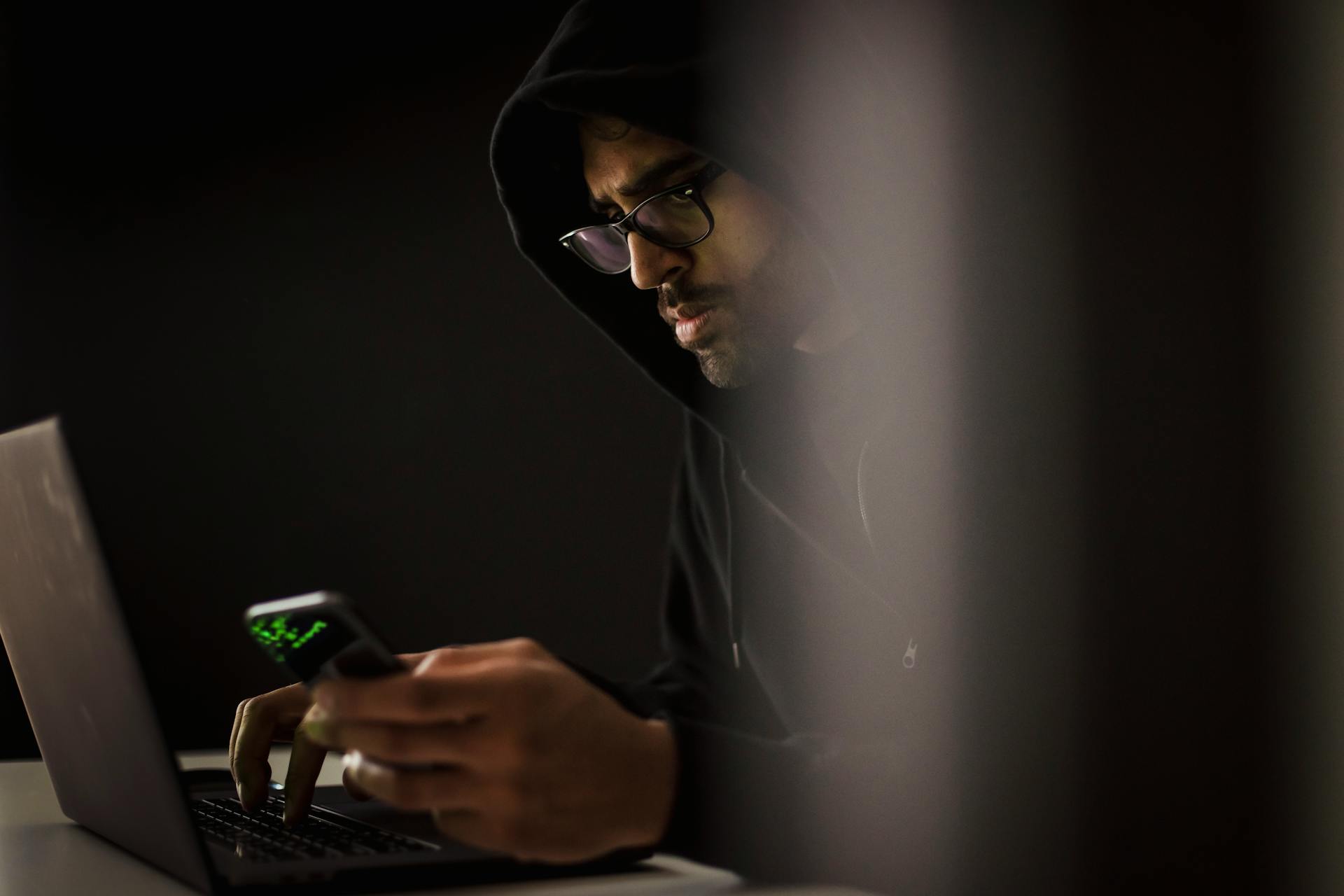 Un homme utilise son smartphone et son ordinateur pour espionner le téléphone de quelqu'un avec l'aide d'une application d'espionnage.
