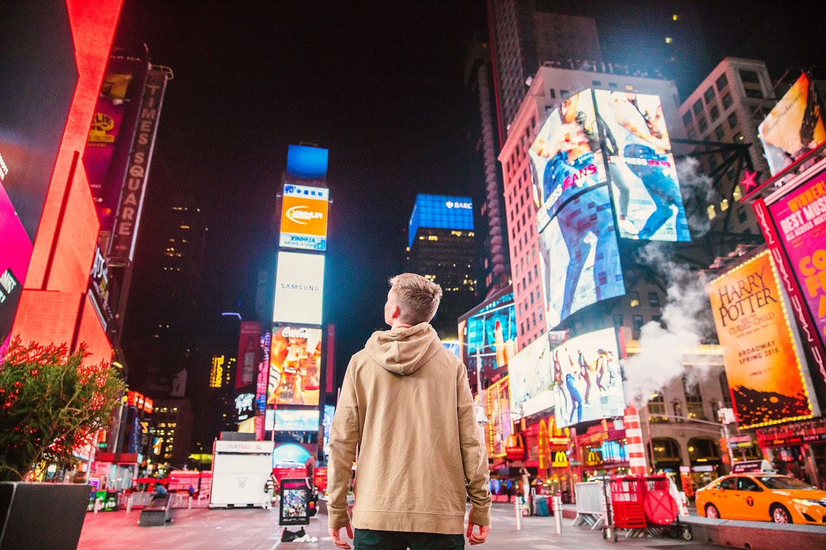homme debout devant des panneaux publicitaires illuminés la nuit