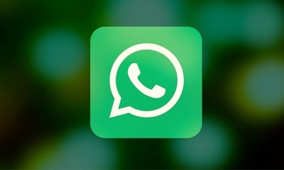 En primer plano de la imagen aparece un logotipo de WhatsApp, con un fondo borroso y verdoso.