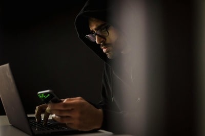 A man uses his smartphone and his computer to spy on someone's telephone with the help of a spying application.

